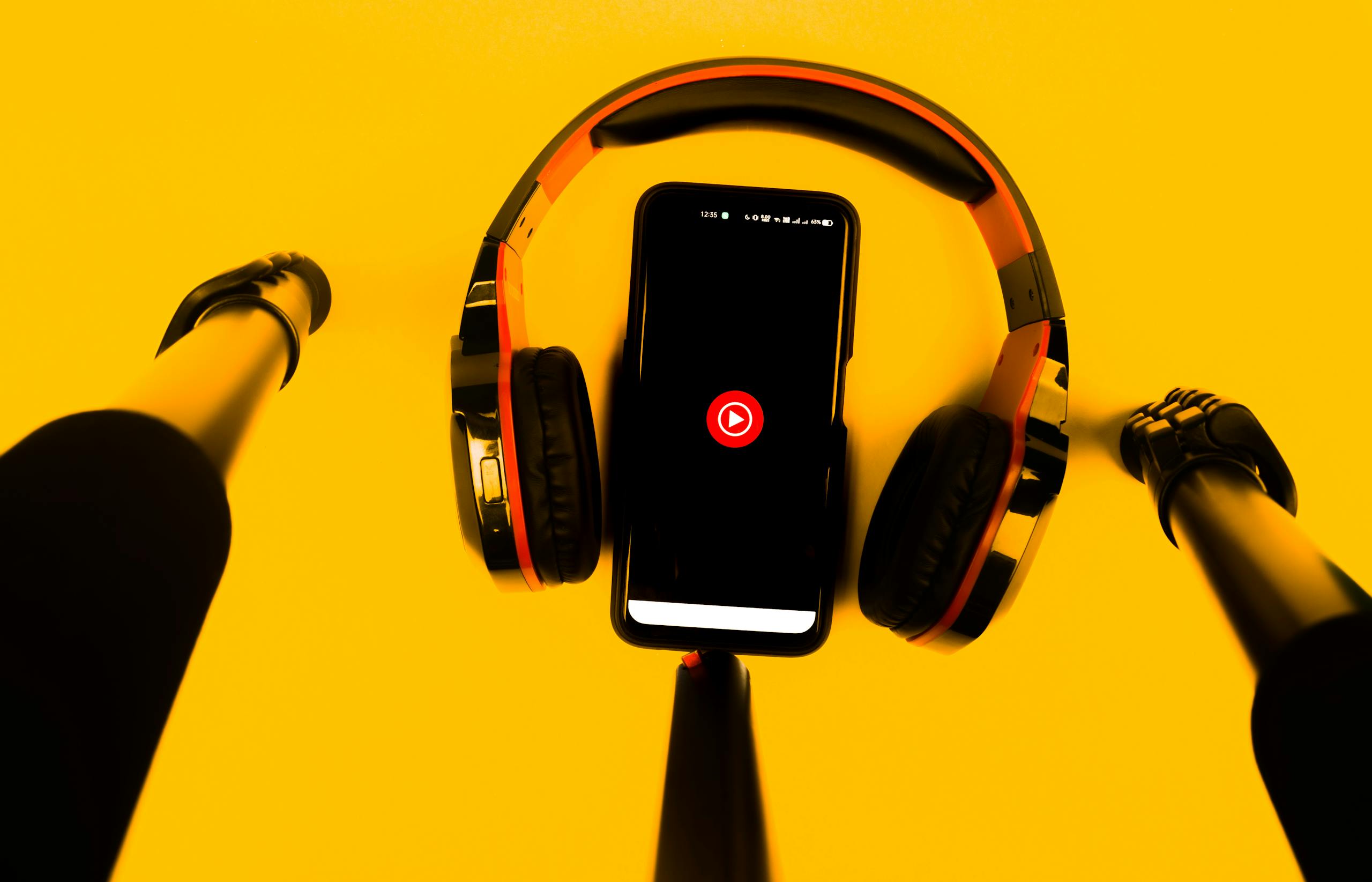 A smartphone with wireless headphones and microphone set against a vibrant yellow background.